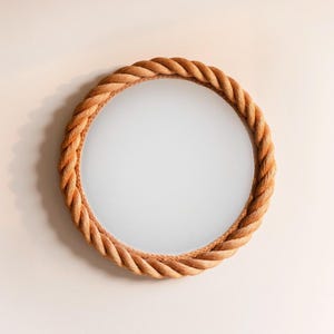 May include: Round mirror with a thick, braided rope frame. The rope is a warm, natural tan color, creating a nautical or coastal aesthetic. The mirror's reflective surface is clear and circular.