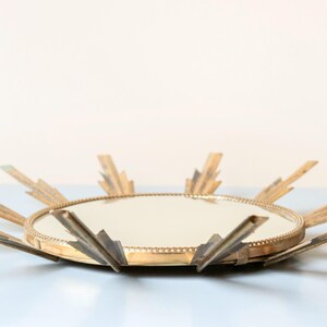 May include: A vintage sunburst mirror with a round mirrored centre and radiating gold-toned metal rays. The mirror has a decorative, mid-century modern design, suitable for wall decor. The overall diameter is approximately 46 cm.