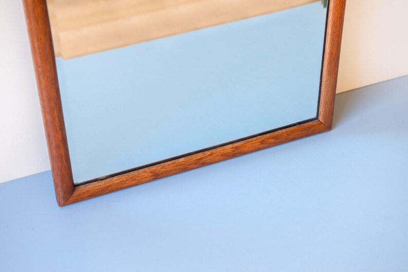 May include: A rectangular wall mirror featuring a medium-toned brown wooden frame with a visible grain pattern. The reflective glass surface is clear and smooth, set within the simple, straight-edged wooden border that surrounds the entire perimeter.