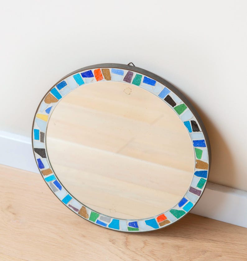 May include: Round mirror with a colorful mosaic tile frame. The frame features blue, green, orange, and white tiles.