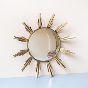 May include: A circular mirror with a gold-coloured sunburst frame. The mirror is round, with a decorative frame featuring textured, pointed rays. A stylish wall mirror, suitable for various interior styles.