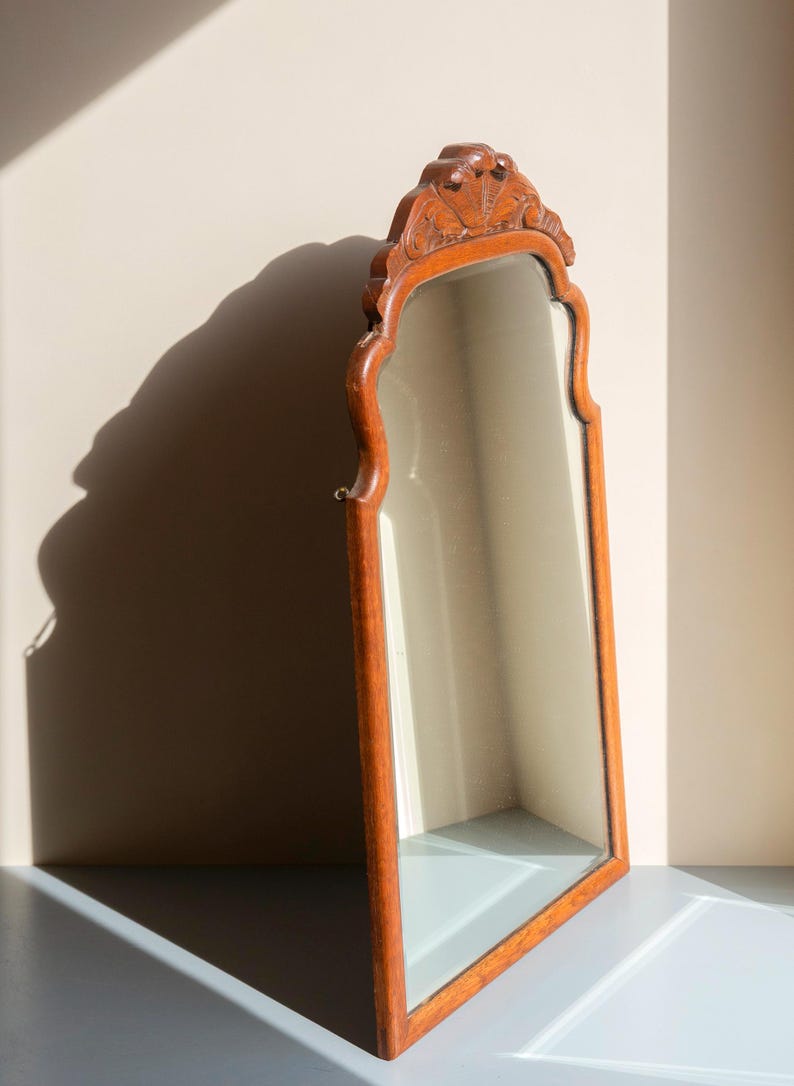 May include: A tall, arched wall mirror featuring a medium-toned wooden frame with a carved, decorative crest at the top. The mirror glass is clear and reflective, set within the smooth, contoured wooden border that follows the arched shape.