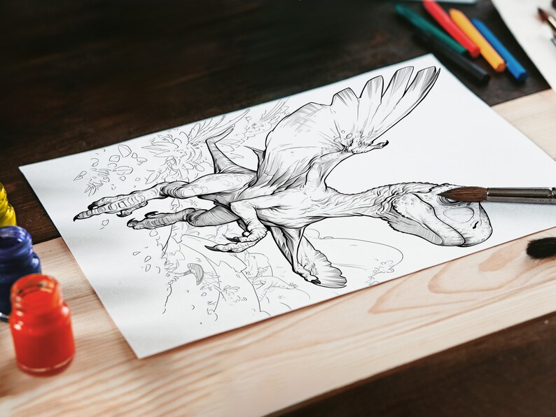 Op de afbeelding: Een zwart-witte lijntekening van een gevleugelde dinosaurus met zijn vleugels uitgespreid. De tekening is op een wit vel papier, dat op een houten tafel ligt. Er staan kwasten en verfpotten op de tafel.