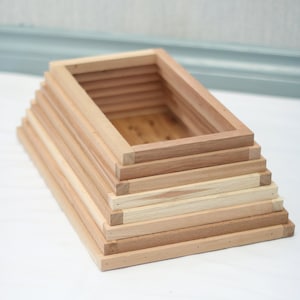 May include: A wooden box made of stacked rectangular frames. The box is made of light brown wood and has a natural finish.