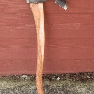 May include: Axe with a wooden handle and a dark metal head. The axe head has a curved design with a sharp blade. The wooden handle is a light brown color.