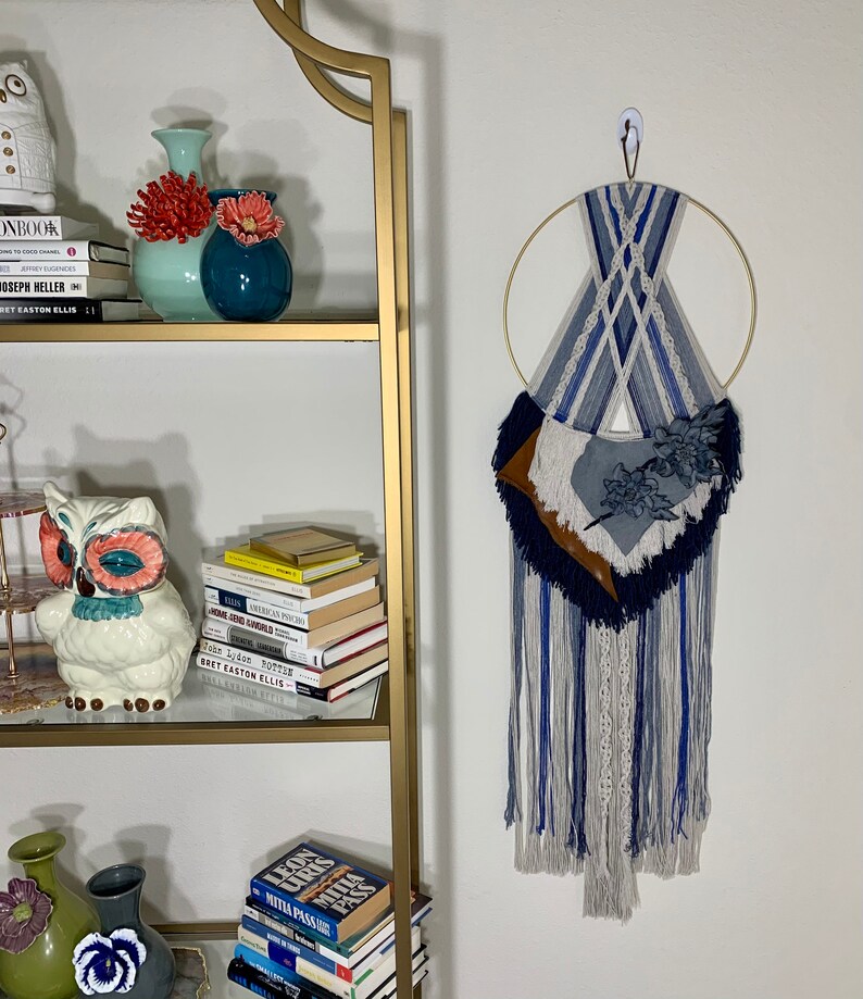 Macrame wall hanging. In shades of denim blues. Created with cotton & shops acrylic yarns, leather hand formed flower with a gold hoop.