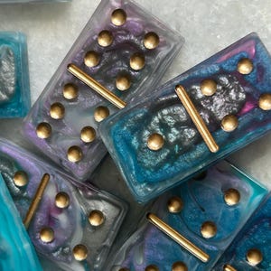 May include: A set of colorful dominoes with gold dots and a gold line down the center. The dominoes have a marbled, iridescent finish.