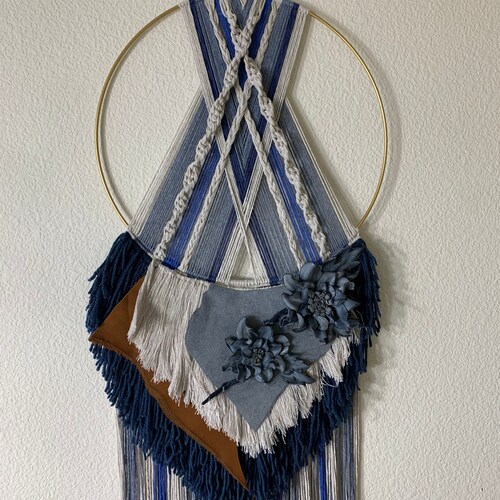 Macrame wall hanging. In shades of denim blues. Created with cotton & shops acrylic yarns, leather hand formed flower with a gold hoop.
