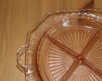 Puede incluir: Un plato de servir de vidrio rosa dividido con un borde festoneado y dos asas. El plato tiene un patrón de rayos de sol y está dividido en tres secciones.