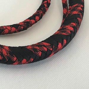 May include: A braided whip with a black and red checkered pattern. The whip is made of a thick, durable material and is designed for use in a variety of settings.