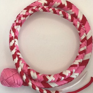 May include: A pink and red braided whip with a white accent. The whip has a pink braided handle.