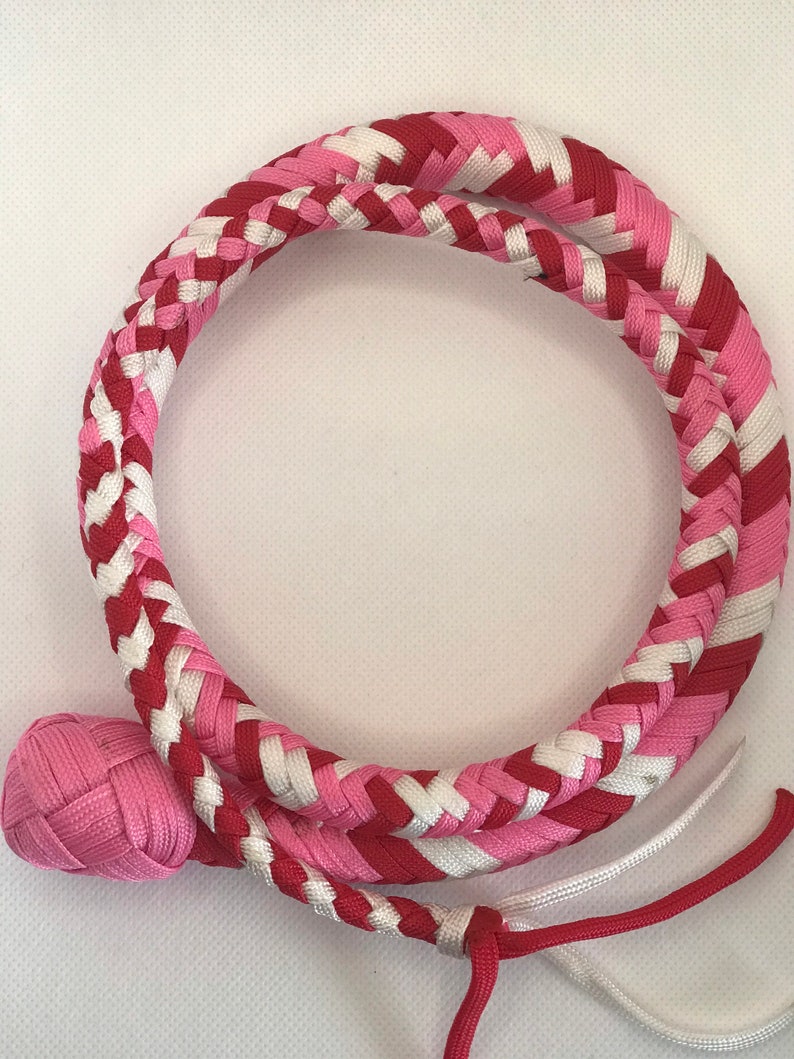 May include: A pink and red braided whip with a white accent. The whip has a pink braided handle.