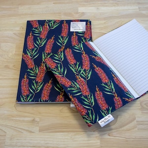 May include: A blue notebook with a floral design cover. The cover features red and green flowers on a dark blue background. The notebook is open to reveal lined pages.