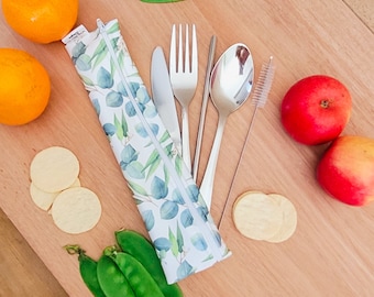 May include: A white and green reusable cutlery set with a zippered pouch. The set includes a fork, knife, spoon, chopsticks, and a cleaning brush. The pouch has a floral pattern.