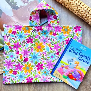 May include: A floral print tote bag with a matching handle, next to a children's book titled "The Three Billy Goats Gruff." The bag features a pattern of pink, blue, and yellow flowers on a white background. A book is open in the background.