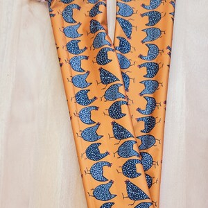 May include: Two long, orange fabric pouches with a repeating pattern of black and white speckled chickens. The pouches have a white drawstring.