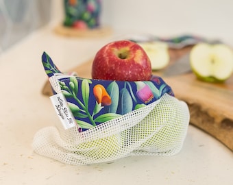 May include: A blue and green floral reusable produce bag with a white mesh net. The bag is filled with apples and has a white tag that says "Little Miss Fi Design".