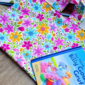 Puede incluir: Un bolso tote floral con un colorido estampado de flores rosas, azules y amarillas. Junto a &eacute;l, un libro infantil titulado "The Three Billy Goats Gruff". La portada del libro presenta ilustraciones de cabras y un trol.