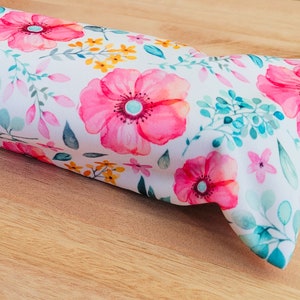 May include: A white fabric with a floral pattern featuring pink, yellow, and green flowers. The fabric is folded in half and has a soft, textured surface.