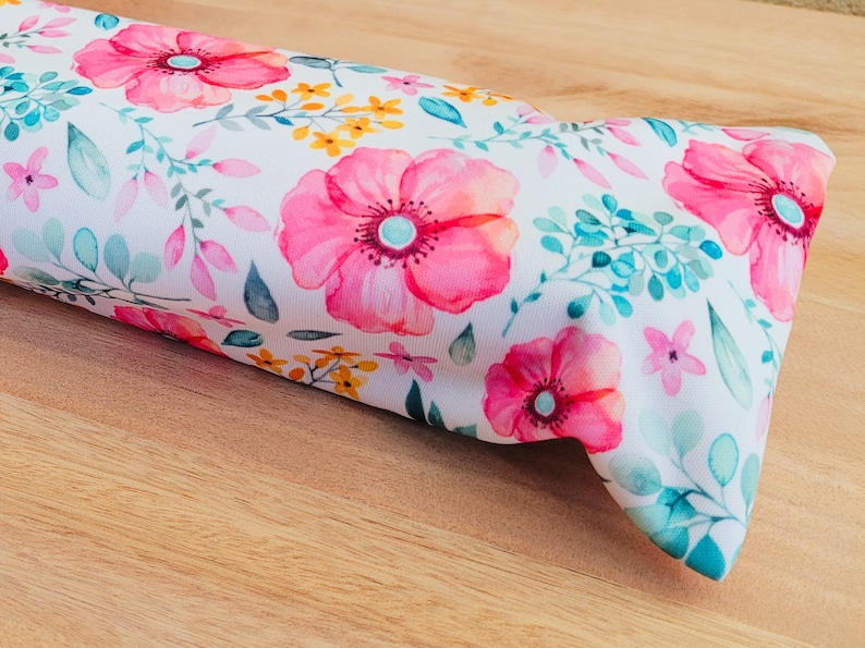 May include: A white fabric with a floral pattern featuring pink, yellow, and green flowers. The fabric is folded in half and has a soft, textured surface.
