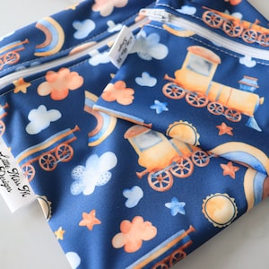 May include: Two blue reusable zippered bags with a train, rainbow, and cloud pattern. The larger bag has a white label that says "Little Miss M Designs".