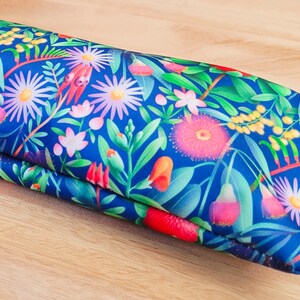 May include: A blue fabric pouch with a floral pattern featuring pink, yellow, and white flowers. The pouch is folded in half and has a smooth, textured surface.