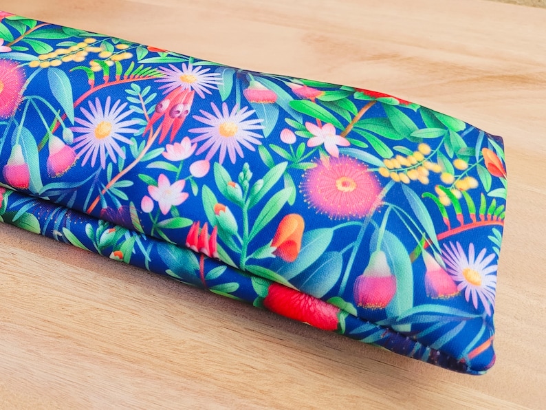 May include: A blue fabric pouch with a floral pattern featuring pink, yellow, and white flowers. The pouch is folded in half and has a smooth, textured surface.