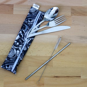 Op de afbeelding: Een zwarte en witte stoffen etui met een ritssluiting die een set roestvrijstalen bestek bevat, waaronder een lepel, een vork, een mes en een rietje met een reinigingsborstel.