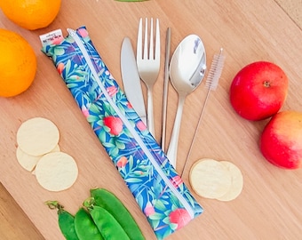 May include: A blue zippered pouch with a floral pattern and a set of stainless steel cutlery, including a fork, knife, spoon, and chopsticks. The pouch is lying on a wooden surface with some fruit and vegetables around it.