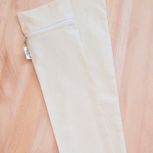 May include: Two off-white canvas zippered pouches. The pouches are lying flat on a light brown wooden surface.