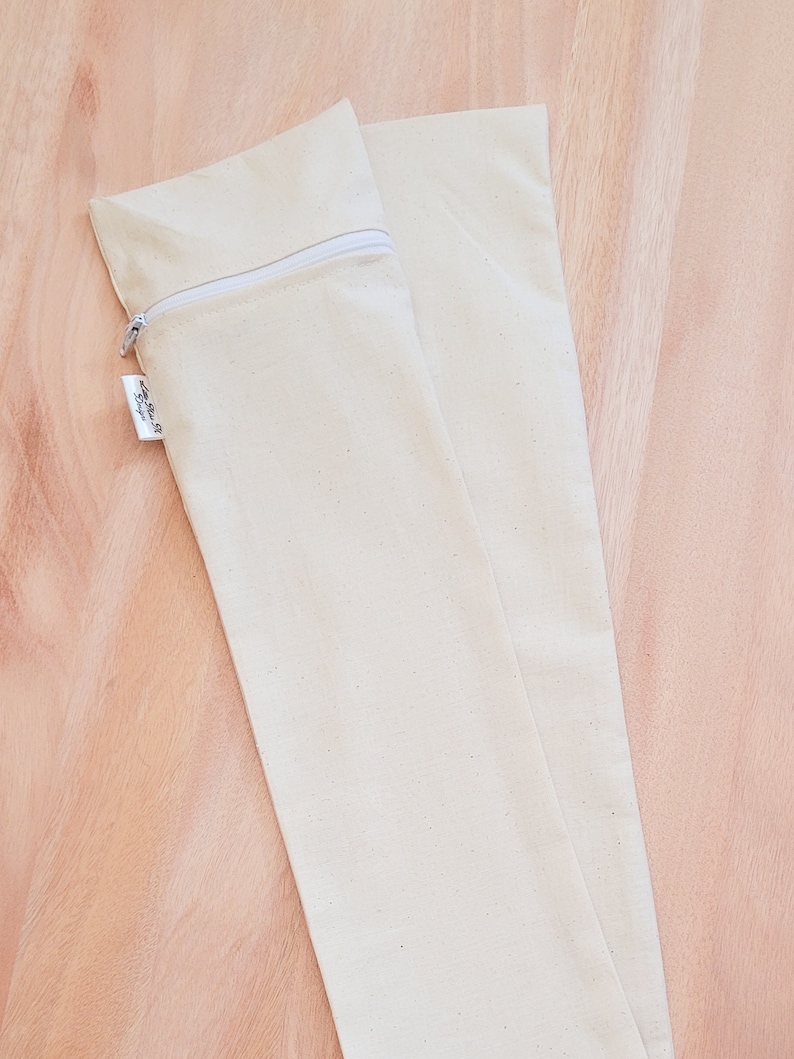 May include: Two off-white canvas zippered pouches. The pouches are lying flat on a light brown wooden surface.