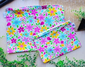 Pode incluir: Duas bolsas reutilizáveis com fecho de correr com padrão floral com flores cor-de-rosa, amarelas, azuis e verdes sobre fundo branco.