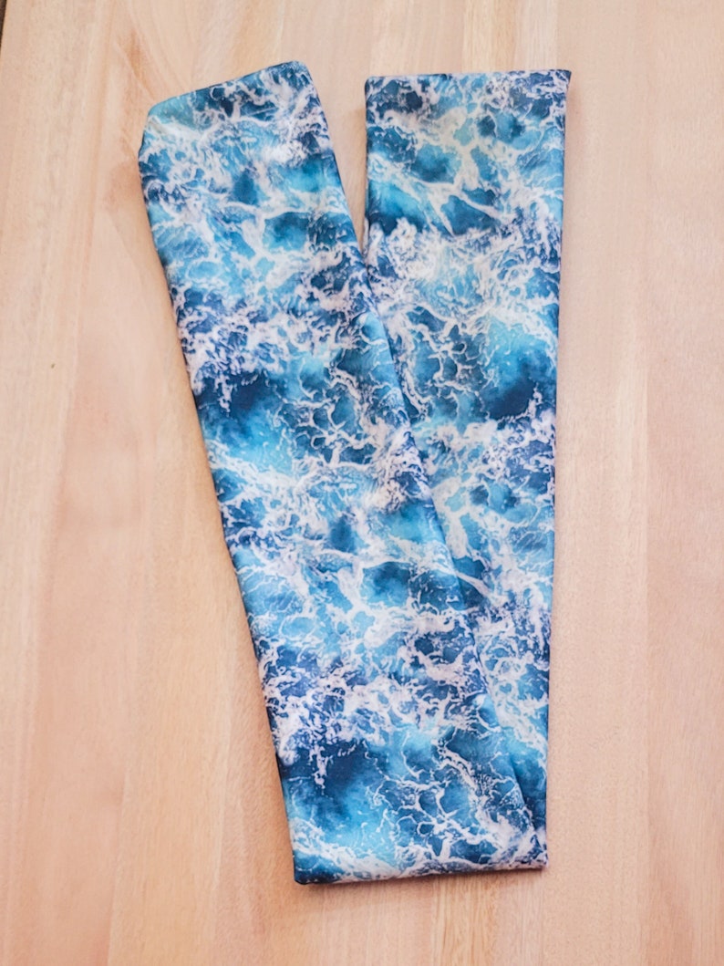 May include: A blue and white fabric with a wave pattern. The fabric is folded in half and is lying on a wooden surface.