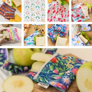May include: Reusable food storage bags with various colourful patterns, including rainbows, flowers, and animals. The bags are made of a waterproof fabric and have a zipper closure. The bags are shown with sandwiches and apples inside.