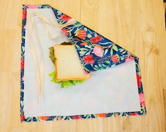 Puede incluir: Una envoltura de tela azul y blanca con un patrón floral con flores rosas. La envoltura está doblada sobre un sándwich.