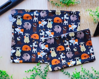 Pode incluir: Duas bolsas de tecido pretas com um padrão repetido de cães de desenho animado em várias cores e poses. A bolsa maior é ligeiramente maior que a menor.