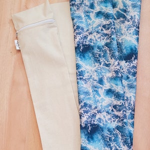May include: Two fabric pouches, one is plain beige with a zipper, the other is blue with a white wave pattern.