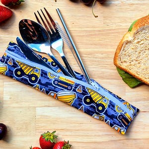 Könnte beinhalten: Eine wiederverwendbare Bestecktasche in Blau und Gelb mit Reißverschluss. Die Tasche ist mit einem Muster aus gelben Kipplastern auf blauem Hintergrund verziert. Die Tasche enthält eine Gabel, einen Löffel, ein Messer und einen Strohhalm.