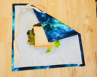 May include: A blue and green patterned fabric wrap with a white trim. The wrap is folded over a sandwich with lettuce and a white bread slice.
