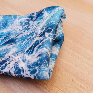 May include: A blue and white fabric with a wave pattern. The fabric is folded and has a soft, silky texture.