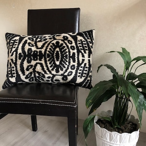 Op de afbeelding: Een rechthoekig sierkussen met een opvallend, symmetrisch ikat-patroon in zwart en cr&egrave;me. Het textiel vertoont complexe, herhalende organische motieven over het hele oppervlak, wat zorgt voor een contrastrijk ontwerp met een geweven textuur.
