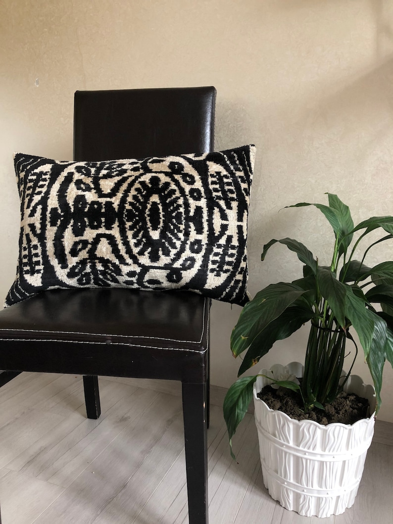 Op de afbeelding: Een rechthoekig sierkussen met een opvallend, symmetrisch ikat-patroon in zwart en cr&egrave;me. Het textiel vertoont complexe, herhalende organische motieven over het hele oppervlak, wat zorgt voor een contrastrijk ontwerp met een geweven textuur.