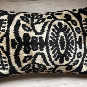 Op de afbeelding: Een rechthoekig sierkussen met een contrastrijk zwart en cr&egrave;me ikat-patroon. Het ontwerp bestaat uit symmetrische, gestileerde bloem- en plantmotieven die in een herhalende, gedurfde grafische lay-out over het gehele oppervlak zijn gerangschikt.