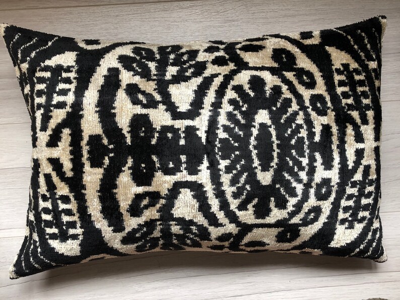 Op de afbeelding: Een rechthoekig sierkussen met een contrastrijk zwart en cr&egrave;me ikat-patroon. Het ontwerp bestaat uit symmetrische, gestileerde bloem- en plantmotieven die in een herhalende, gedurfde grafische lay-out over het gehele oppervlak zijn gerangschikt.
