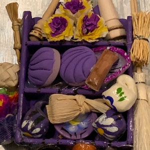 Può includere: Uno scaffale in legno viola con vari oggetti, tra cui un'immagine religiosa, una scopa, un mattarello di legno, fiori viola e gialli, pane viola, un bastone marrone, un'anfora in ceramica bianca e un vaso in ceramica marrone.