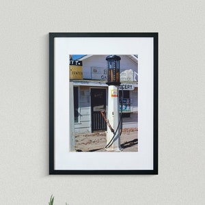 May include: A black and white photograph of a vintage gas pump in front of a small building with a sign that reads "City Center Garage". The building also has a sign that reads "Grocery".