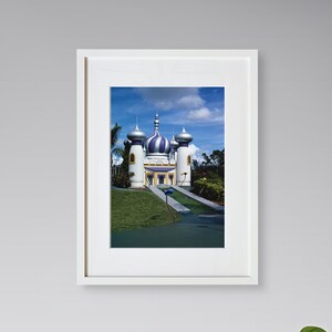 May include: A white building with blue and purple domes, surrounded by green grass and trees. The building has a walkway leading to the entrance.