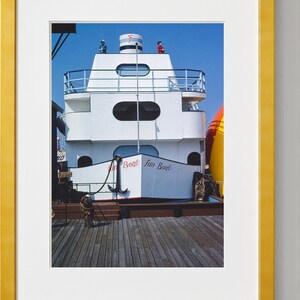 May include: A white boat with red lettering that says "Fun Boat" docked at a pier. The boat has a red and white striped top and a black anchor on the front.