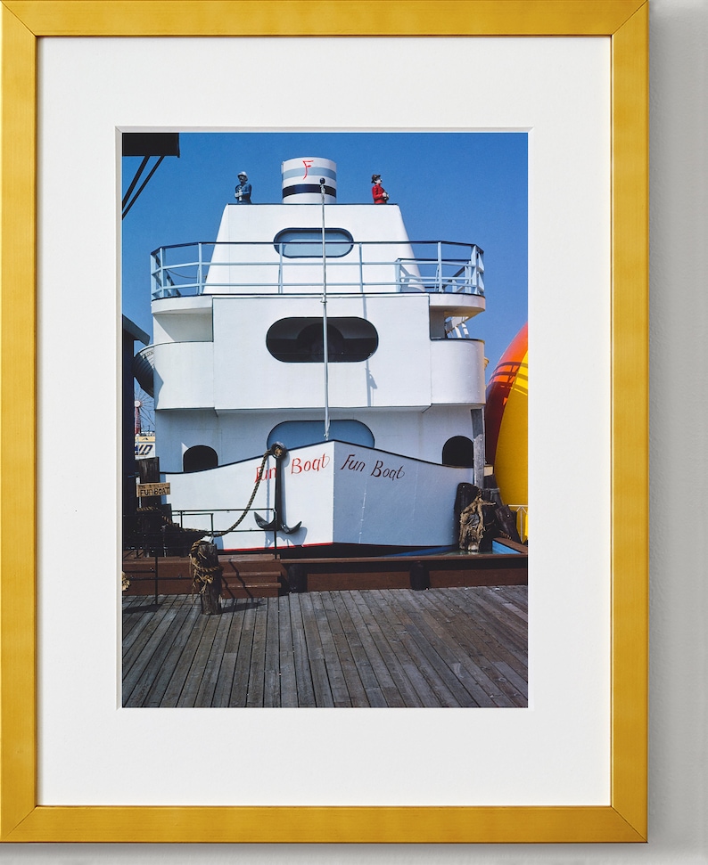 May include: A white boat with red lettering that says "Fun Boat" docked at a pier. The boat has a red and white striped top and a black anchor on the front.