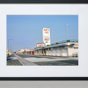 May include: A vintage photograph of a boardwalk with a sign for Hunt's Pier Skyline Golf and a building labelled "Ocean Centre".